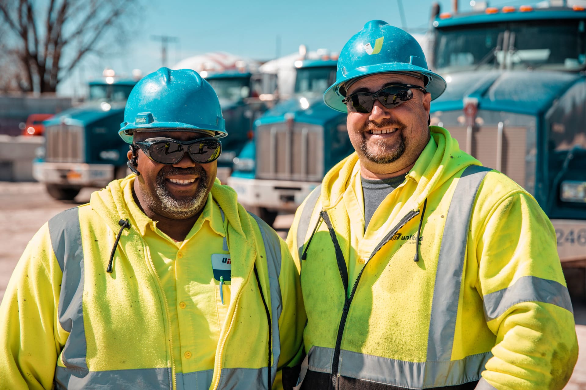 DelaySet - two smiling United Materials drivers in hard hats and hi-vis jackets in front of mixer trucks