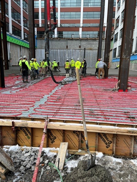 FiberMaxFI - crew pumping concrete over red in-floor radiant heating tubing on an urban jobsite