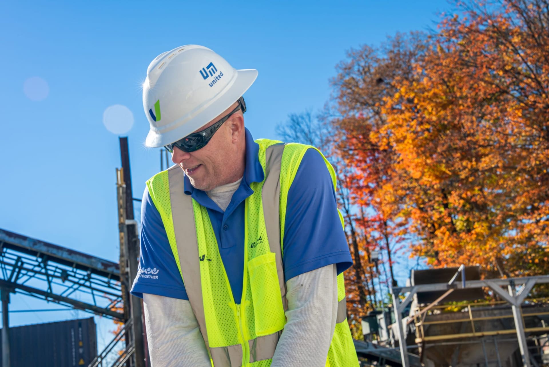 Get-Set - worker in a white hard hat and safety vest at the plant with autumn trees behind